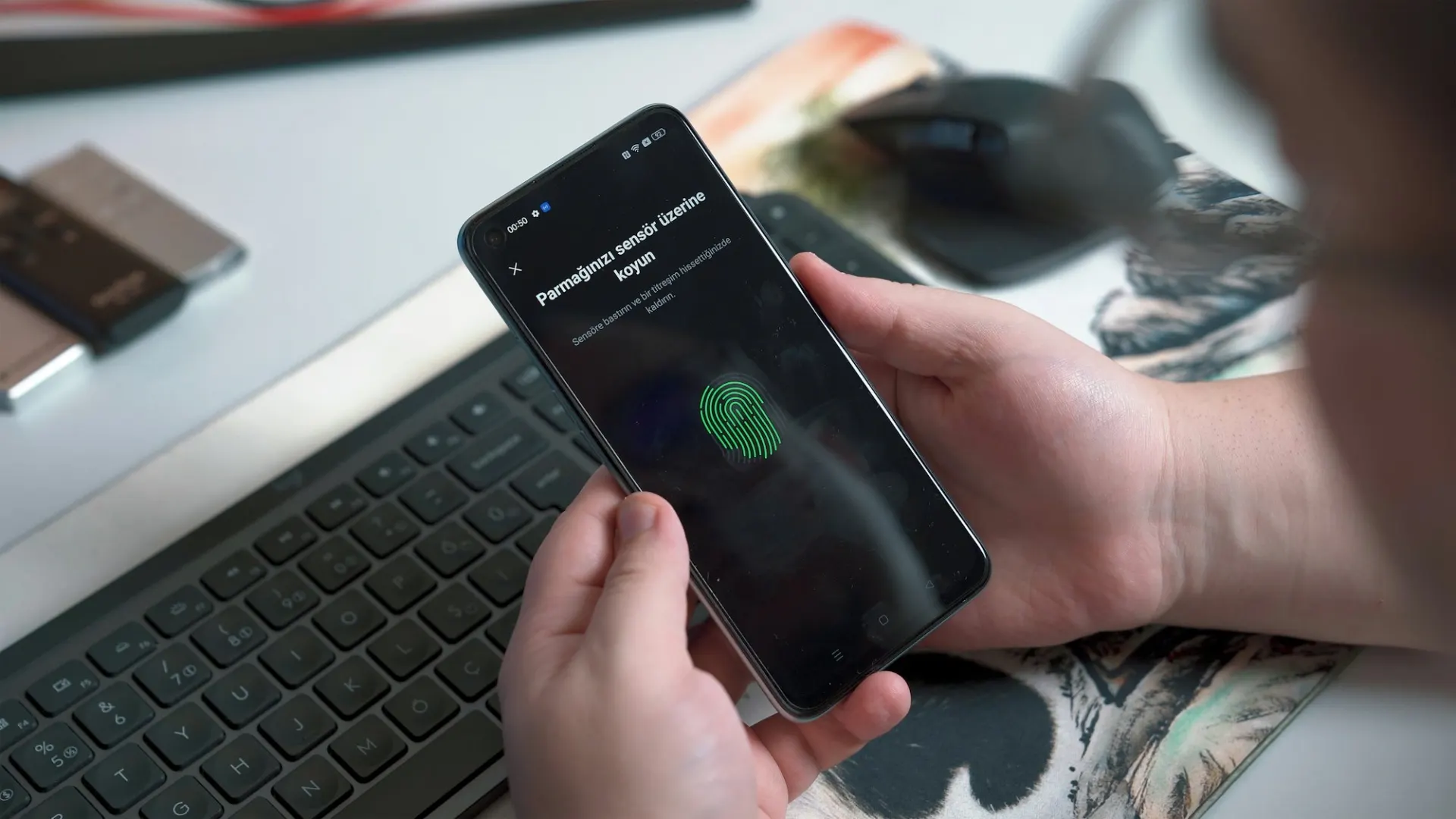 Handen met een smartphone die om een vingerafdruk vraagt, boven een laptop